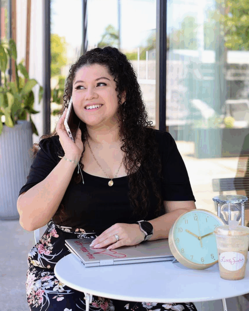 A woman sitting at a cafe smiling while on her phone